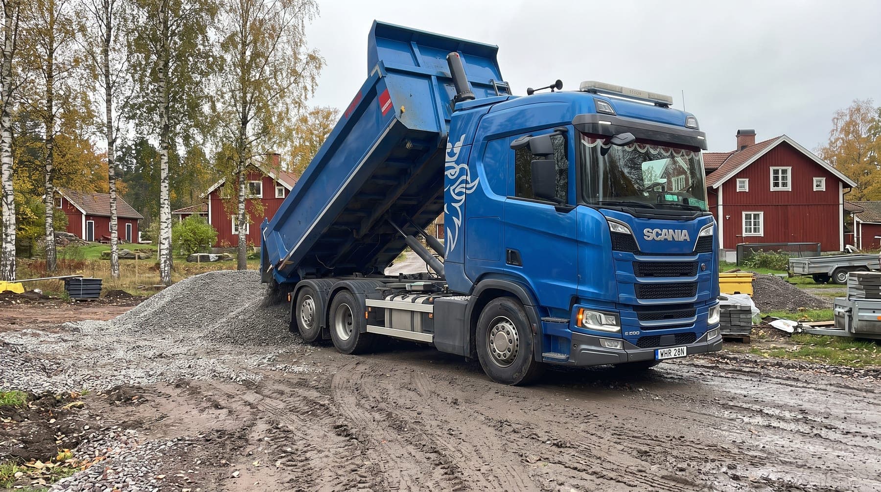 Blå Scania med tippflak som tippar krossmaterial vid ett villabygge